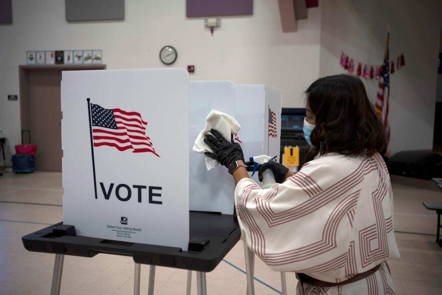 An election worker cleans a polling booth with an American flag on it