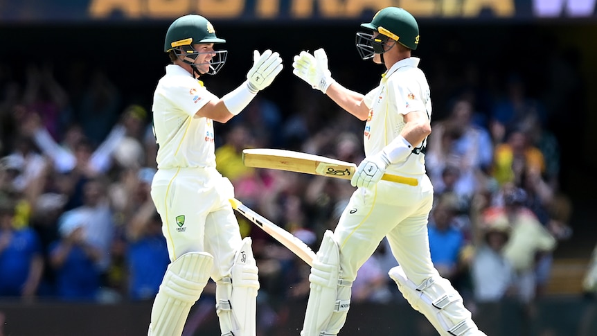 Two Australian male batters prepare to shake hands as they celebrate winning the first Ashes Test.