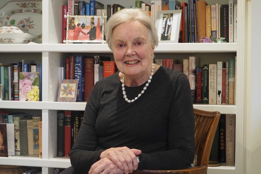 Former South Australia Liberal MP Jennifer Cashmore sits in her lounge room with photos and books on a shelf behind her