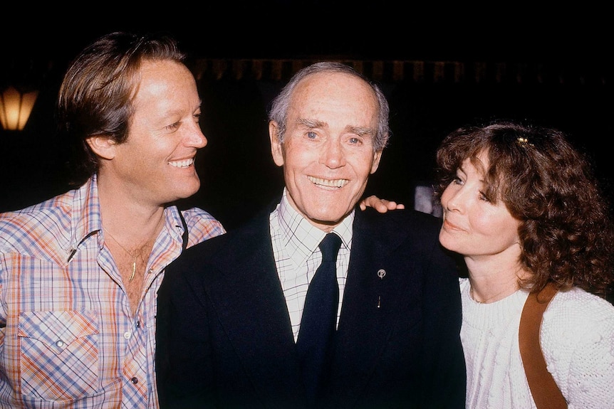 Peter Fonda puts his hand on his father Henry's shoulder and smiles at him. On Henry Fonda's other side is Shirlee Fonda.