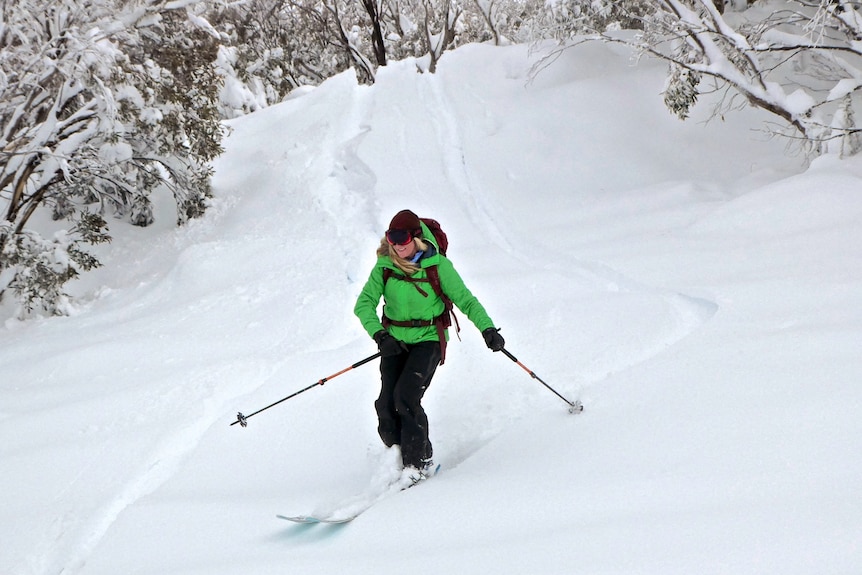 A woman in a green jacket goes skiing.