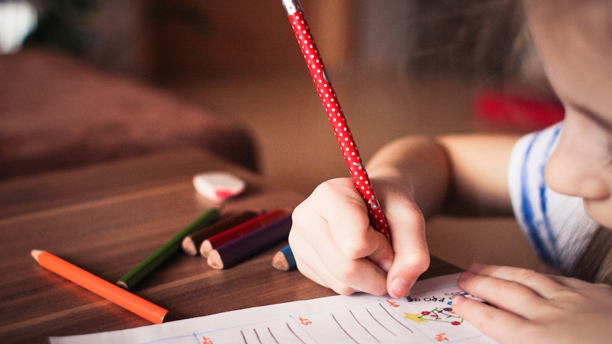 A young child draws at a desk using brightly coloured pencils