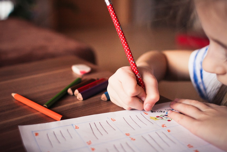 A young child draws at a desk using brightly coloured pencils