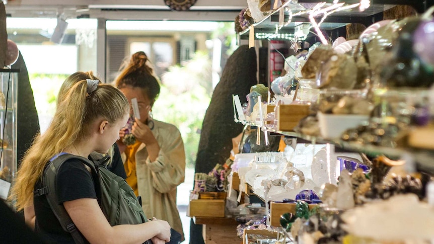 A group of shoppers gaze at a store shelf full of crystals.