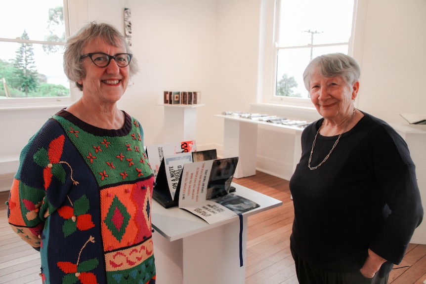 Two women stand in a gallery space surrounded by art works.