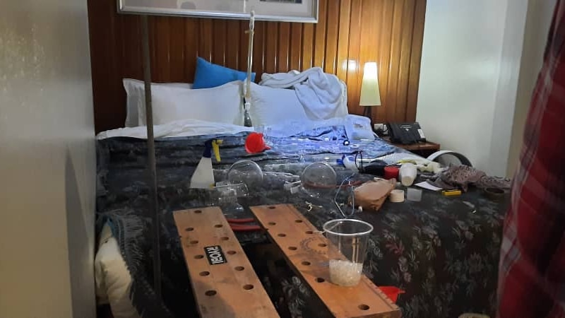 Equipment scattered across a bed in a hotel room. There is a cup with a white substance in it, in the foreground.