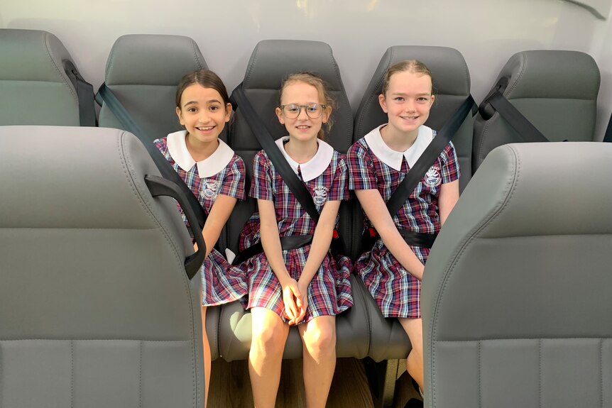 three children sitting on a bus smiling