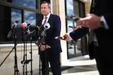 WA Premier Mark McGowan stands in front of a row of media microphones.