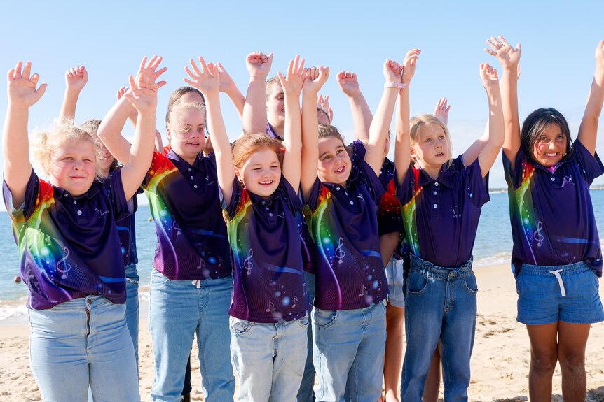 a group of young girls all smiling with their hands in the air on a beach