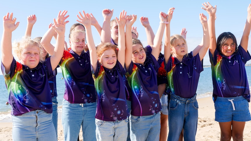 a group of young girls all smiling with their hands in the air on a beach
