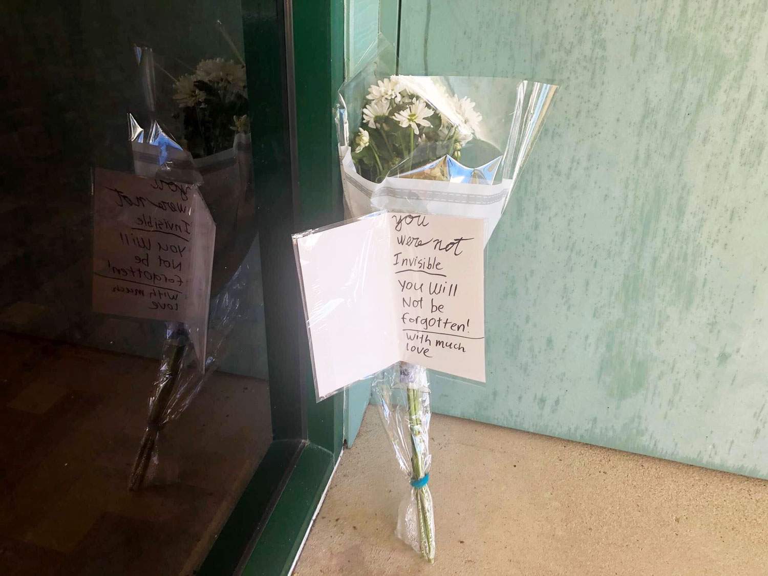 Floral tribute with message 'you were not invisible, you will not be forgotten! With much love' placed outside community centre.