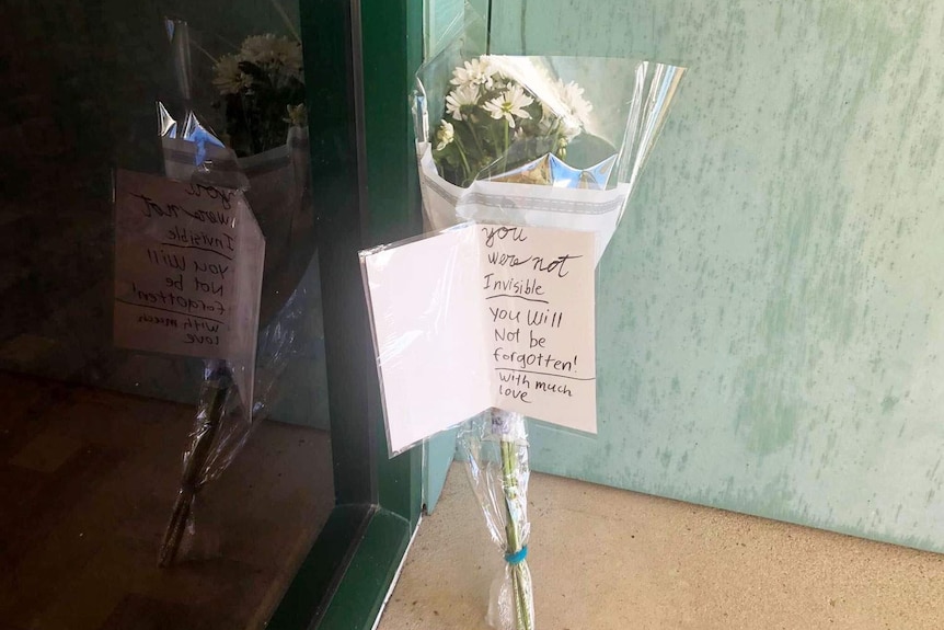 Floral tribute with message 'you were not invisible, you will not be forgotten! With much love' placed outside community centre.