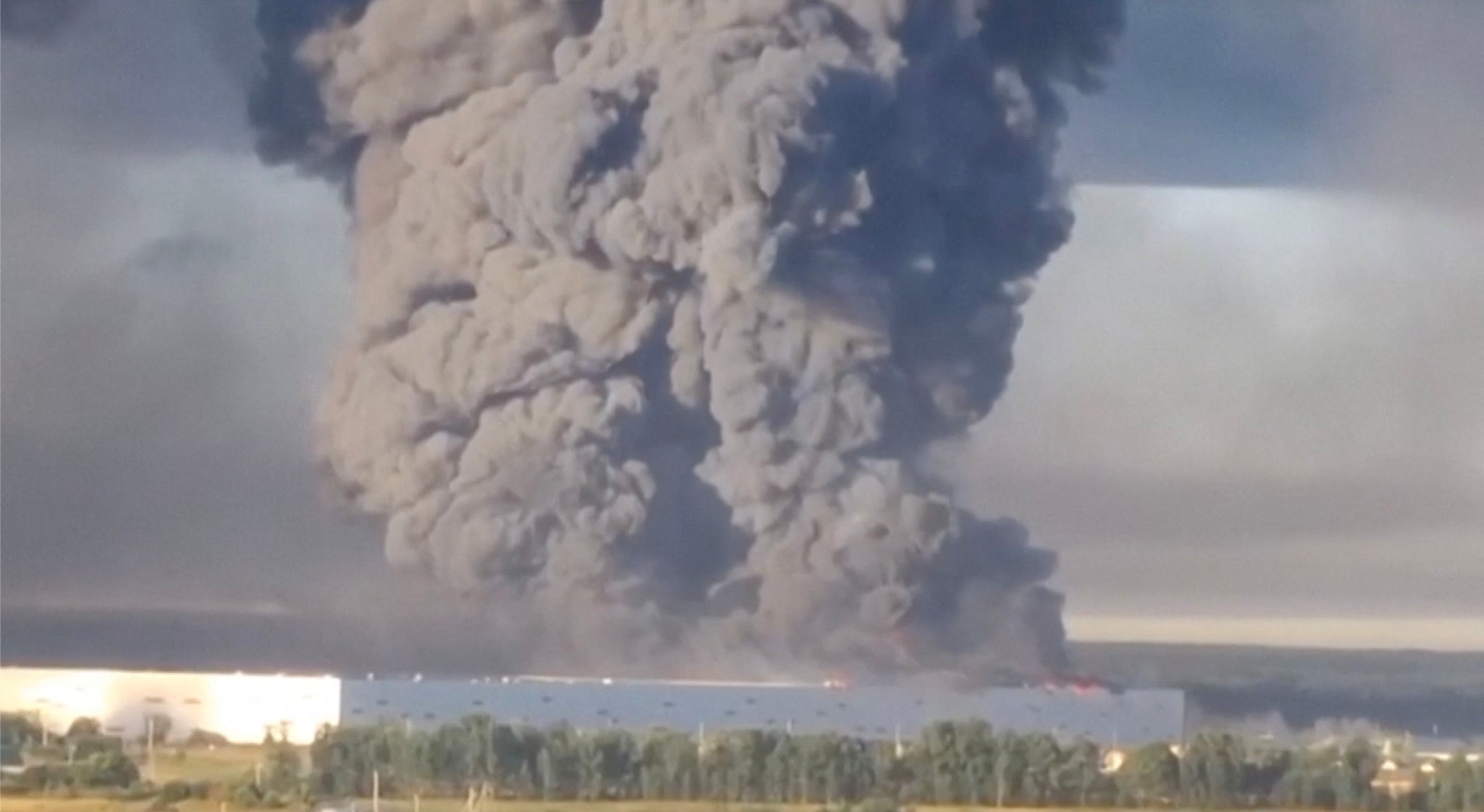 Huge plumes of grey smoke rise in to the sky from a fire at a warehouse.