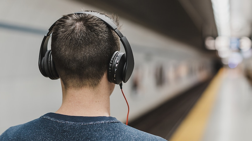 A man stands on a platform listening through headphones.