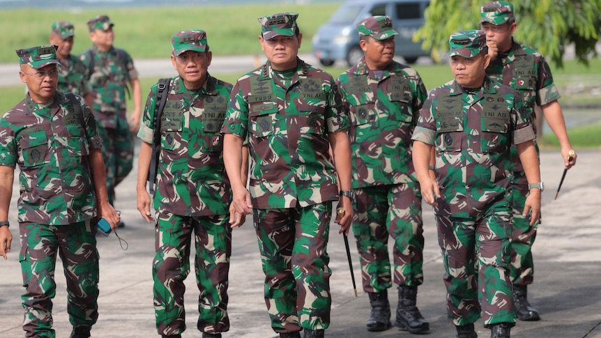 A group of eight men walk together in camo military outfits along a road.