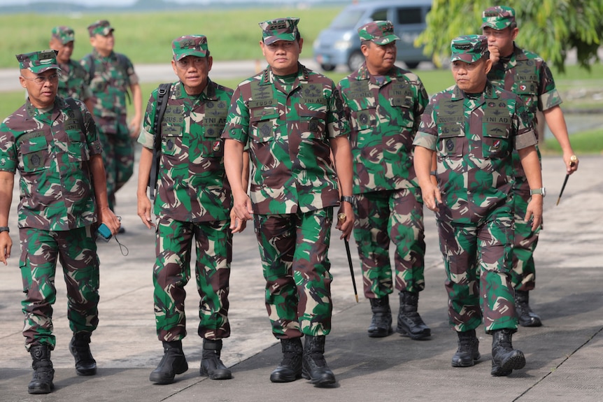 A group of eight men walk together in camo military outfits along a road.