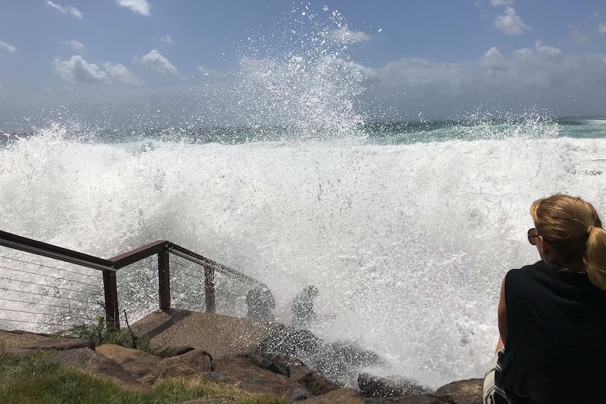 A big wave crashes onto people sitting on stairs down to the beach at Snapper Rocks.