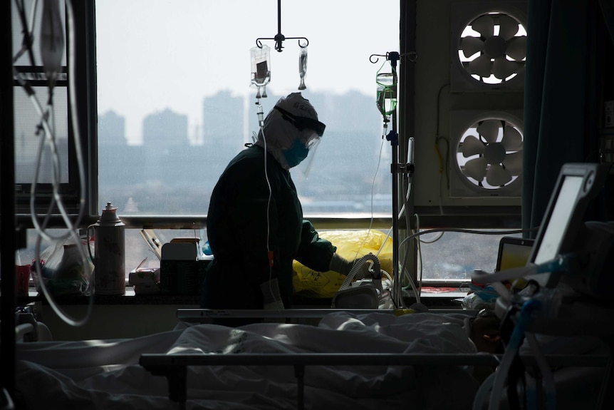 A medical worker in protective suit attends to a patient in an isolated ward of a hospital in Wuhan.