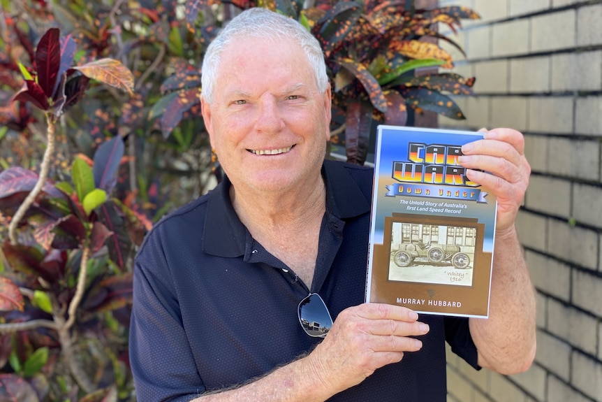 Man holding up a book titles Car Wars Down Under.