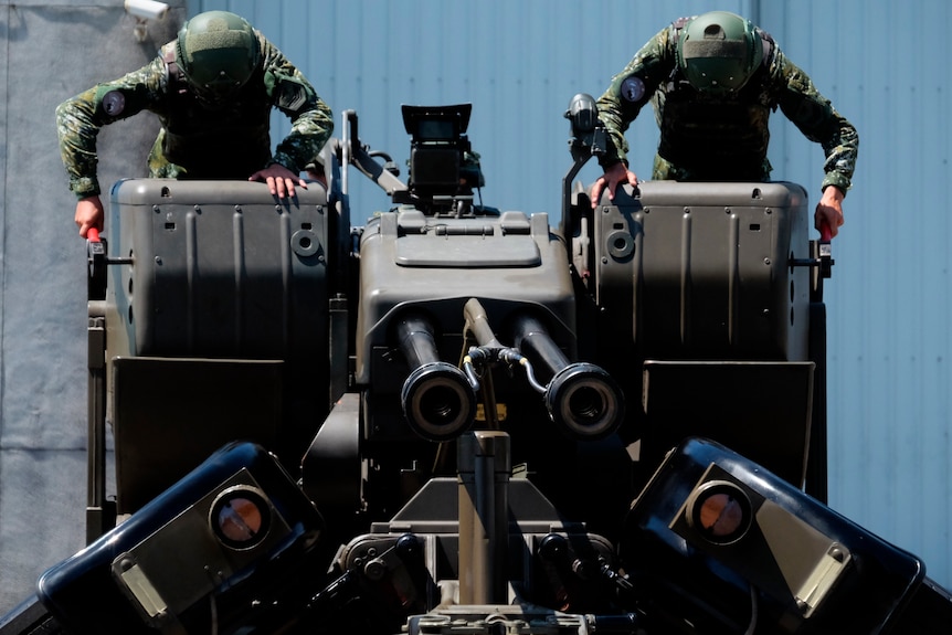 Two Taiwanese soldiers wearing camouflage and green helmets sit atop a large anti-aircraft gun, working levers.