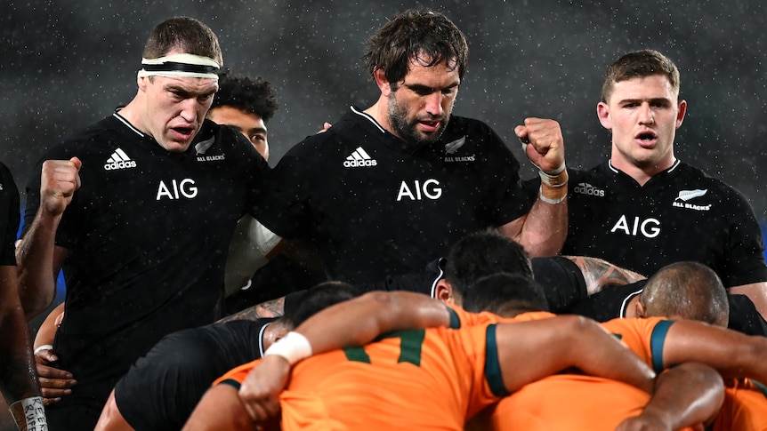 Two All Blacks stand up behind a scrum with their fists clenched