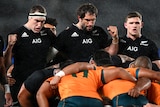 Two All Blacks stand up behind a scrum with their fists clenched