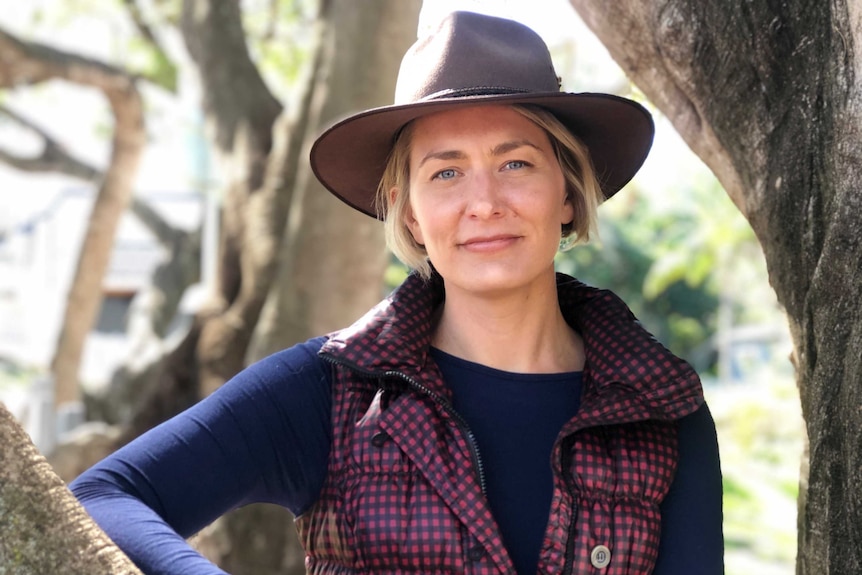 Sophia Walters stands between tree trunks wearing a hat.