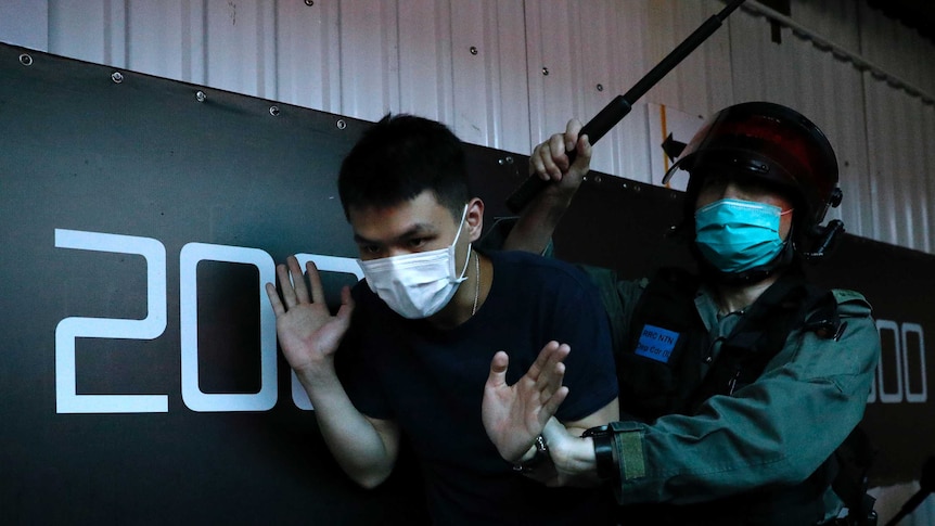 A detained anti-government protester is held by a riot police officer during a march in Hong Kong.