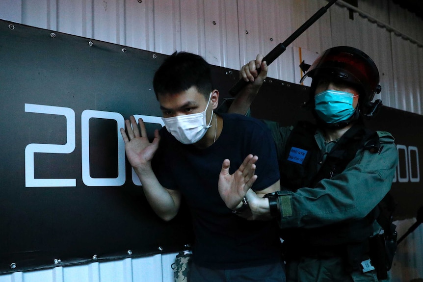 A detained anti-government protester is held by a riot police officer during a march in Hong Kong.