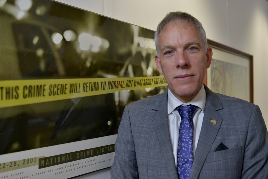 A man ion a suit standing beside a crime scene poster.
