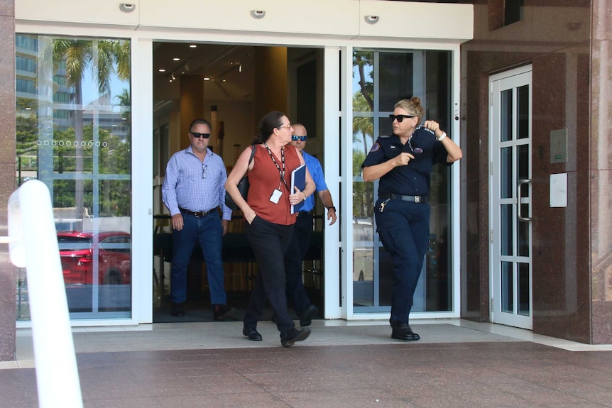 Two police officers, one in uniform, leave Darwin Supreme Court. They are talking to each other and look serious.