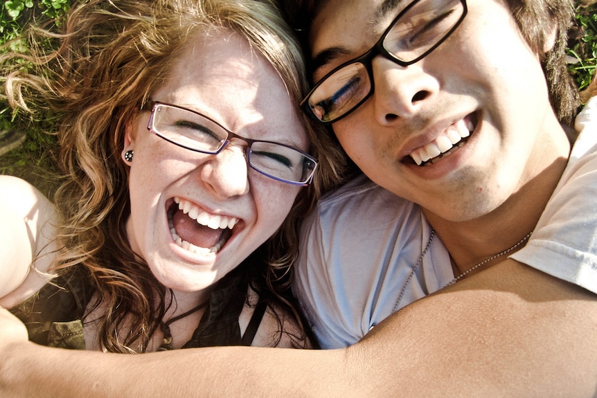 A woman and man lying on the grass, hugging.