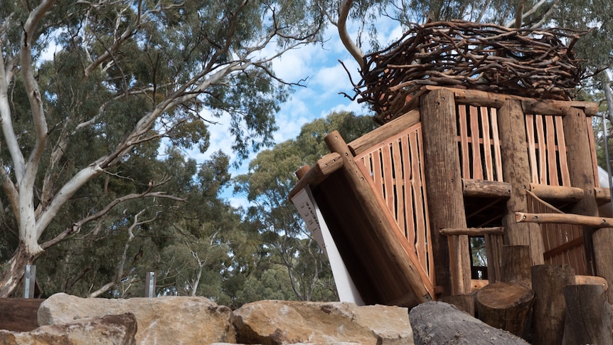 A tree fort tower with a slide, surrounded by rocks and a large tree trunk.