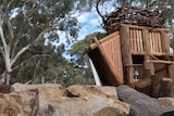A tree fort tower with a slide, surrounded by rocks and a large tree trunk.