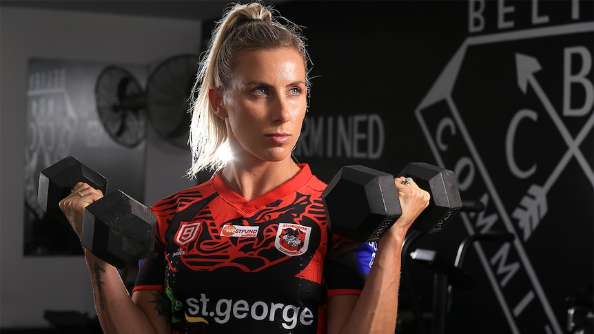 Sam Bremner holds two dumbbells inside a gym, wearing her St George Illawarra Dragons uniform.