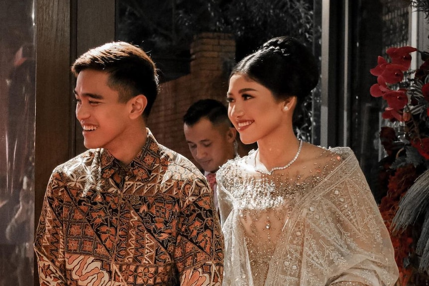 An Indonesian man in a traditional shirt walks with a woman in an evening gown