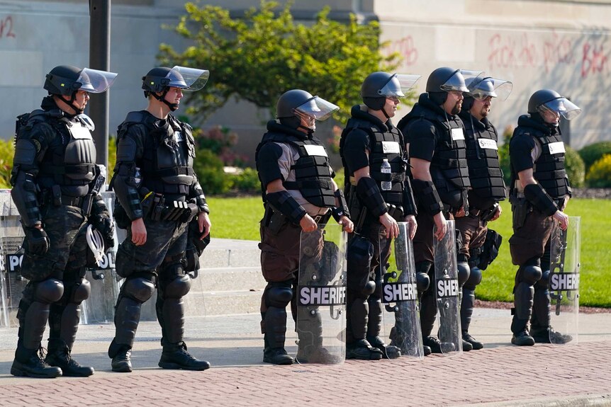 Police in riot gear stand outside the Kenosha County Court House in daylight.