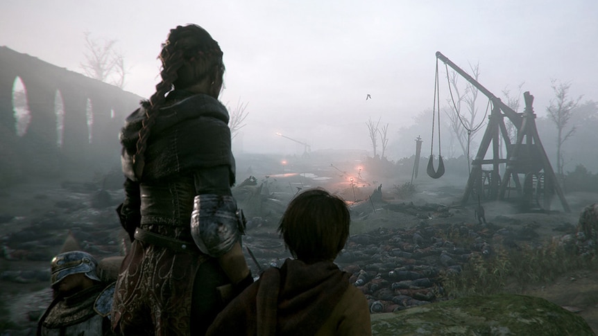 Two video game characters viewed from behind look toward a medieval catapault.
