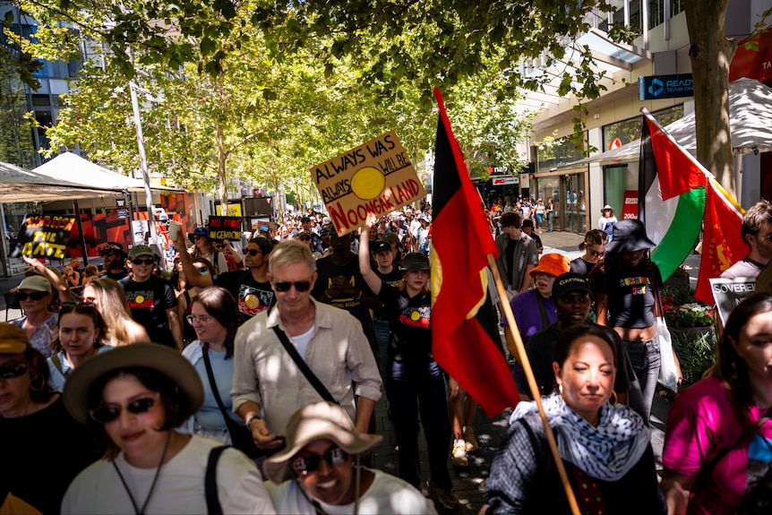 A crowd of protesters carrying flags and signs as part of an Invasion Day rally. 