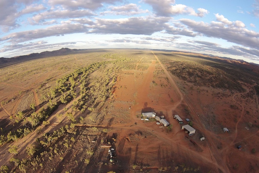 Pine Hill Station aerial view with fish-eye lens shows a dozen sheds and buildings, red dirt, low vegetation and distant ranges