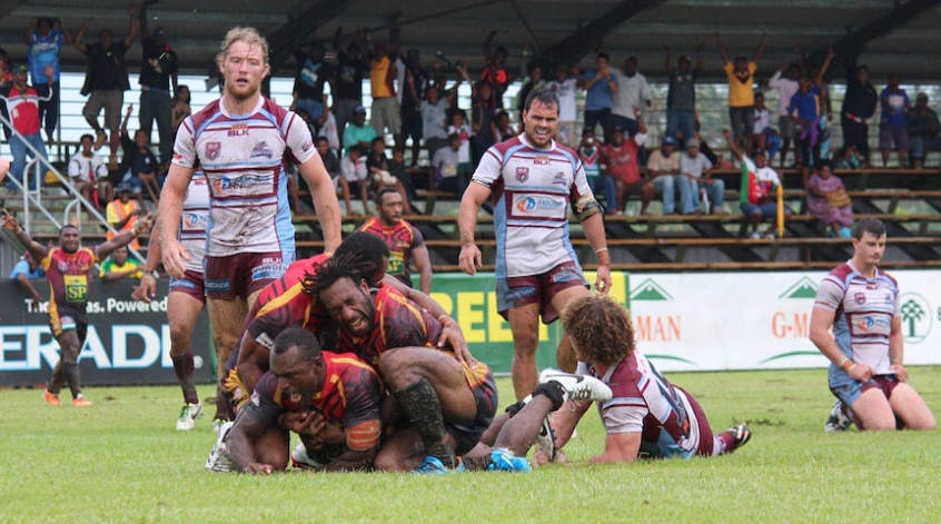 A group of football players embracing on the ground after a try