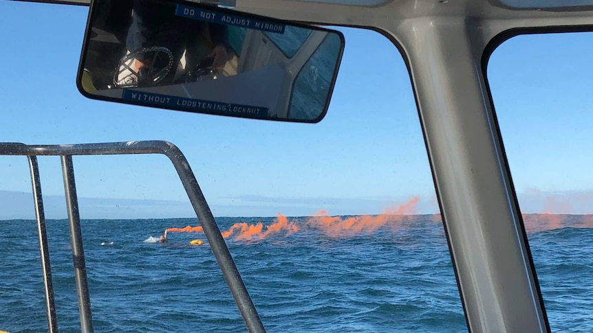 picture of man holding a smoking orange flare in the water, clinging onto a dinghy.