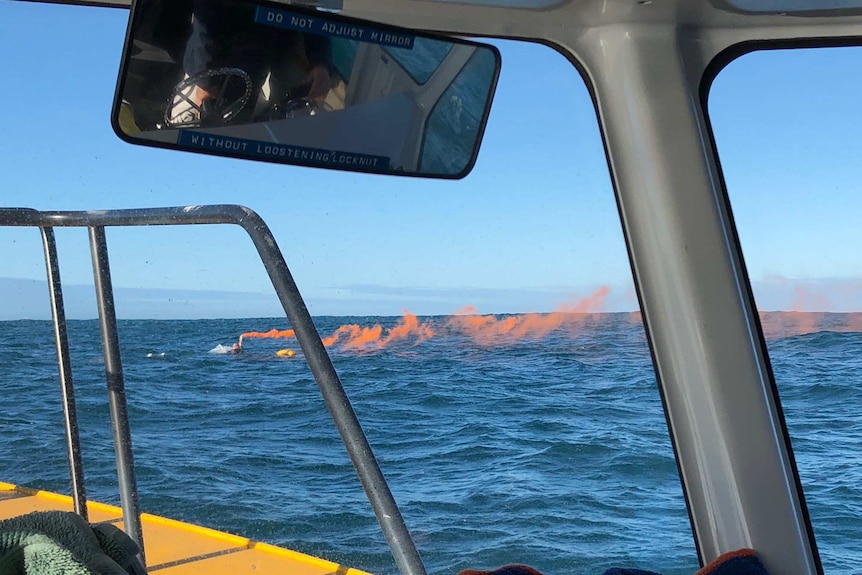 picture of man holding a smoking orange flare in the water, clinging onto a dinghy.