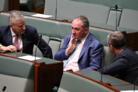 Three men sitting on government benches deep in conversation.