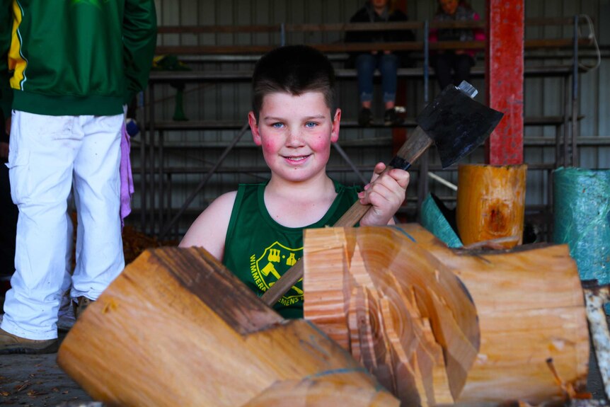 young boy holding axe smiling in front of chopped log