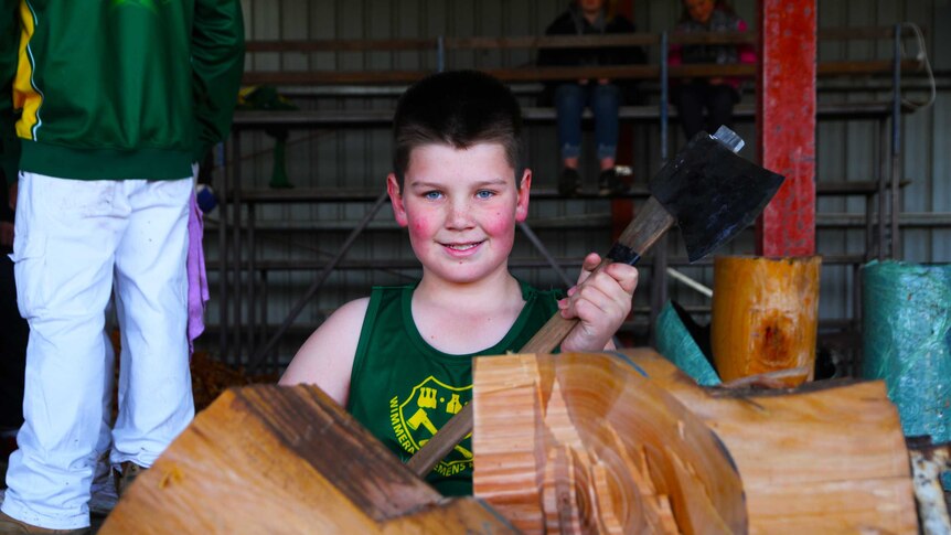 young boy holding axe smiling in front of chopped log