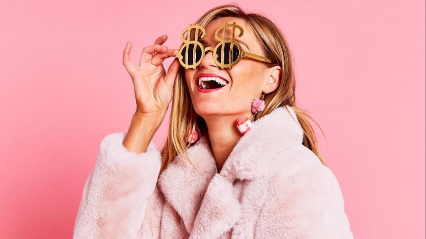 Woman in a pink fur coat wearing gold glasses with dollar signs on the front of the frames.