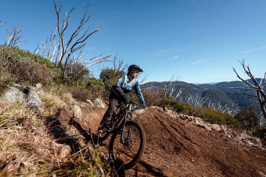 A woman on a bike going down a hill with mountains in the background. 