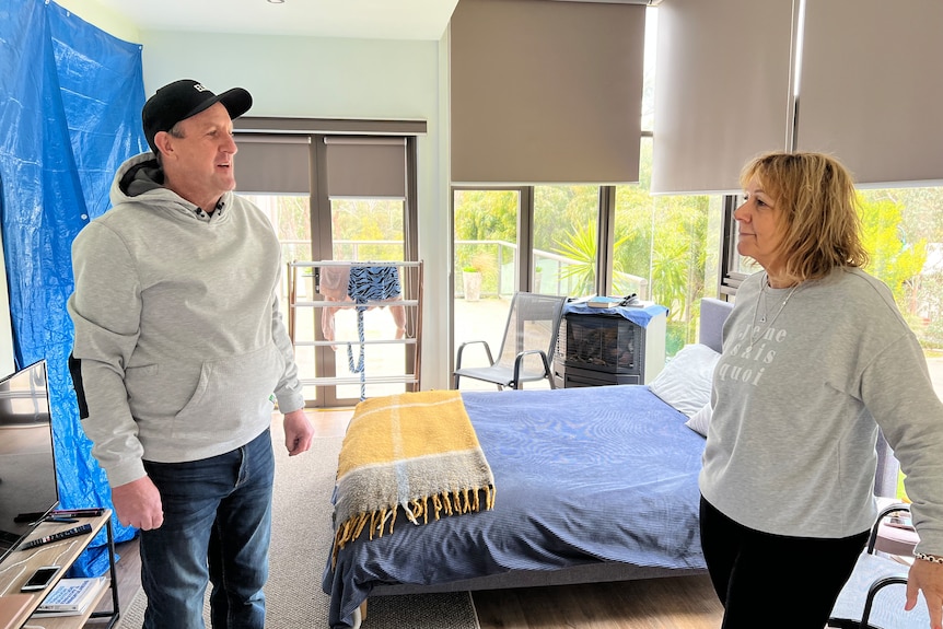 couple stand in storm-damaged bedroom of home