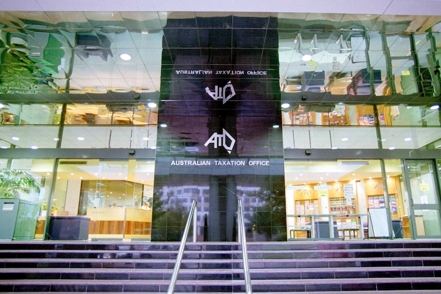 The imposing glass facade of an office building with lettering that reads "Australian Taxation Office".